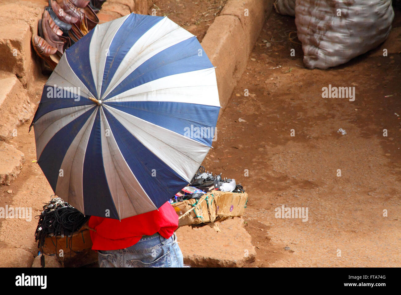 A market vendor stands by his merchandise completely covered in a large white and blue umbrella. Stock Photo
