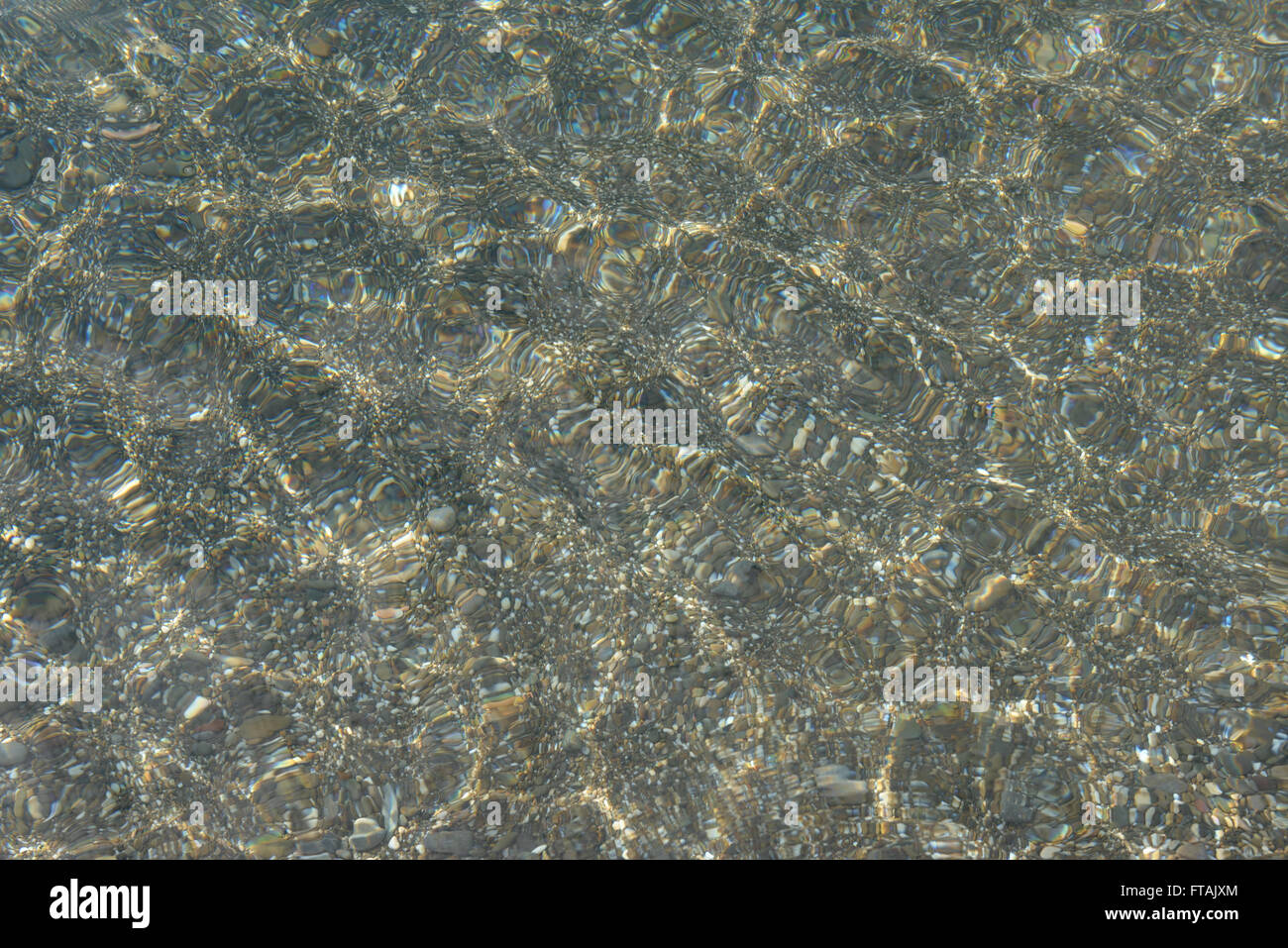 Shimmering sun glares on pebble seabed under clear water of shallow of ...