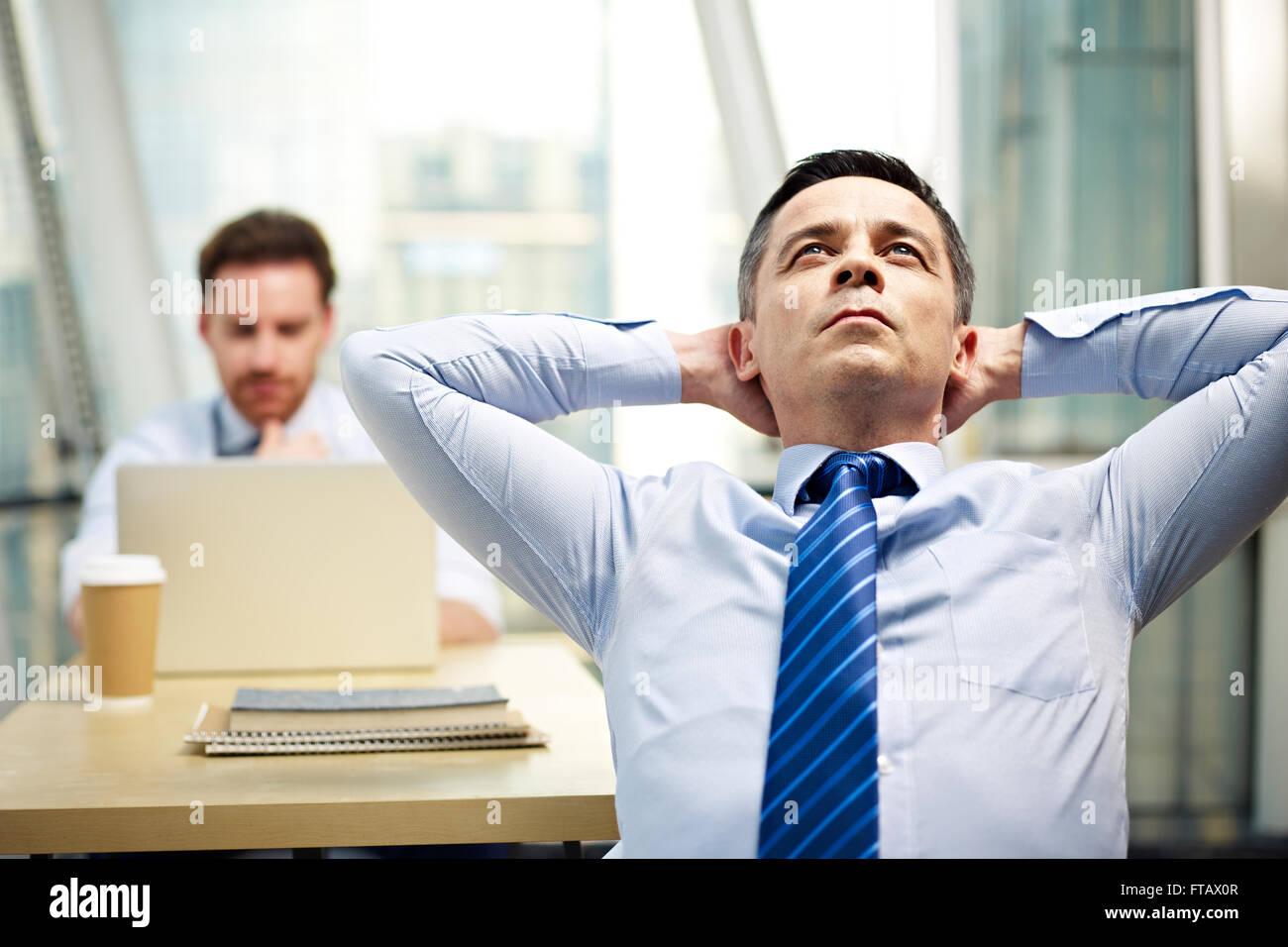 businessman sitting in office hands behind head thinking Stock Photo ...