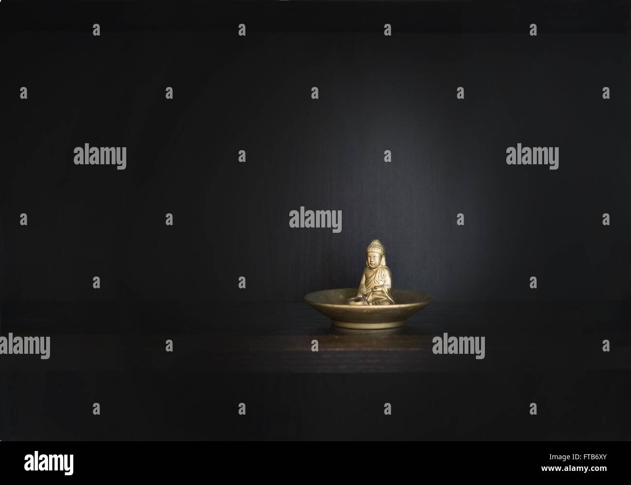Gold metal Buddha on dark background with copy space, chiaroscuro style. Stock Photo