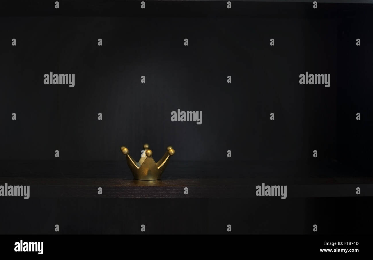 Gold metal crown on dark background with copy space, chiaroscuro style. Stock Photo