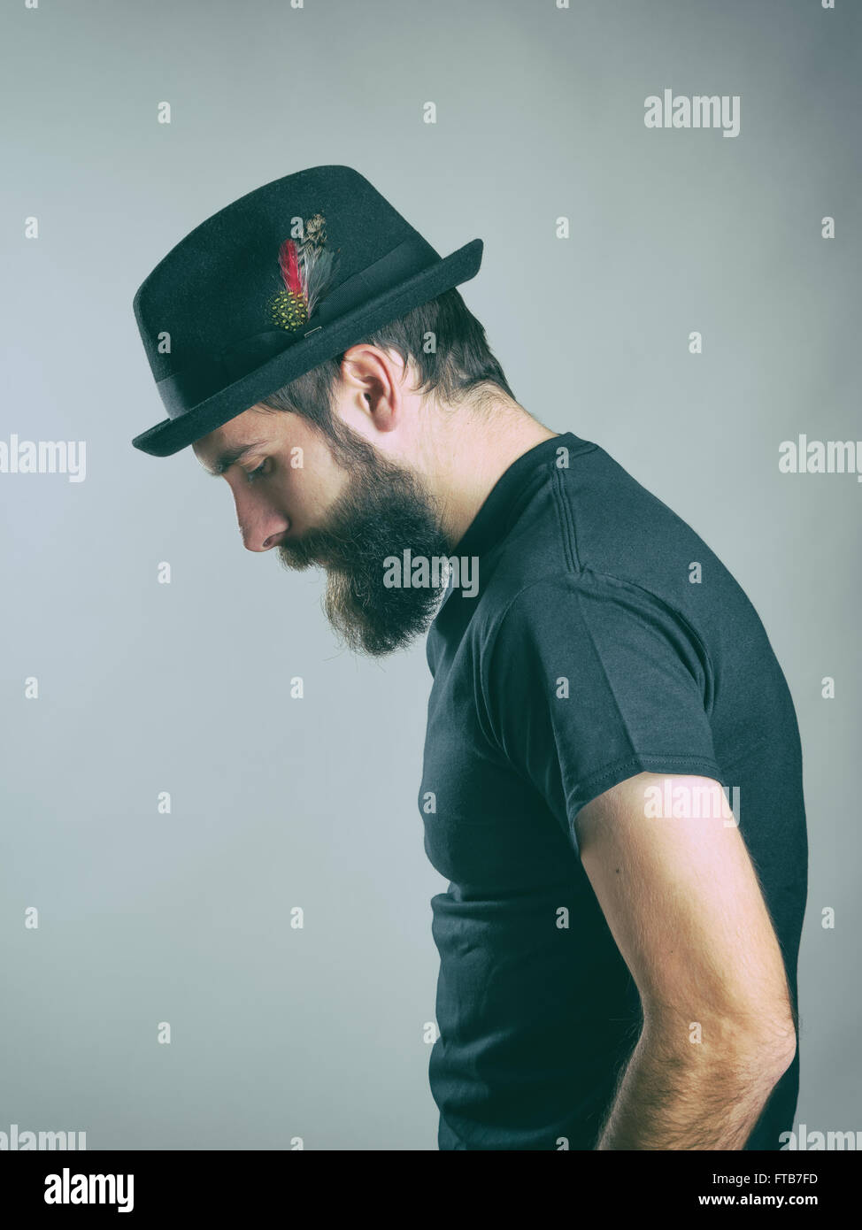 Side view of sad hunched bearded man with hat looking down. Retro toned