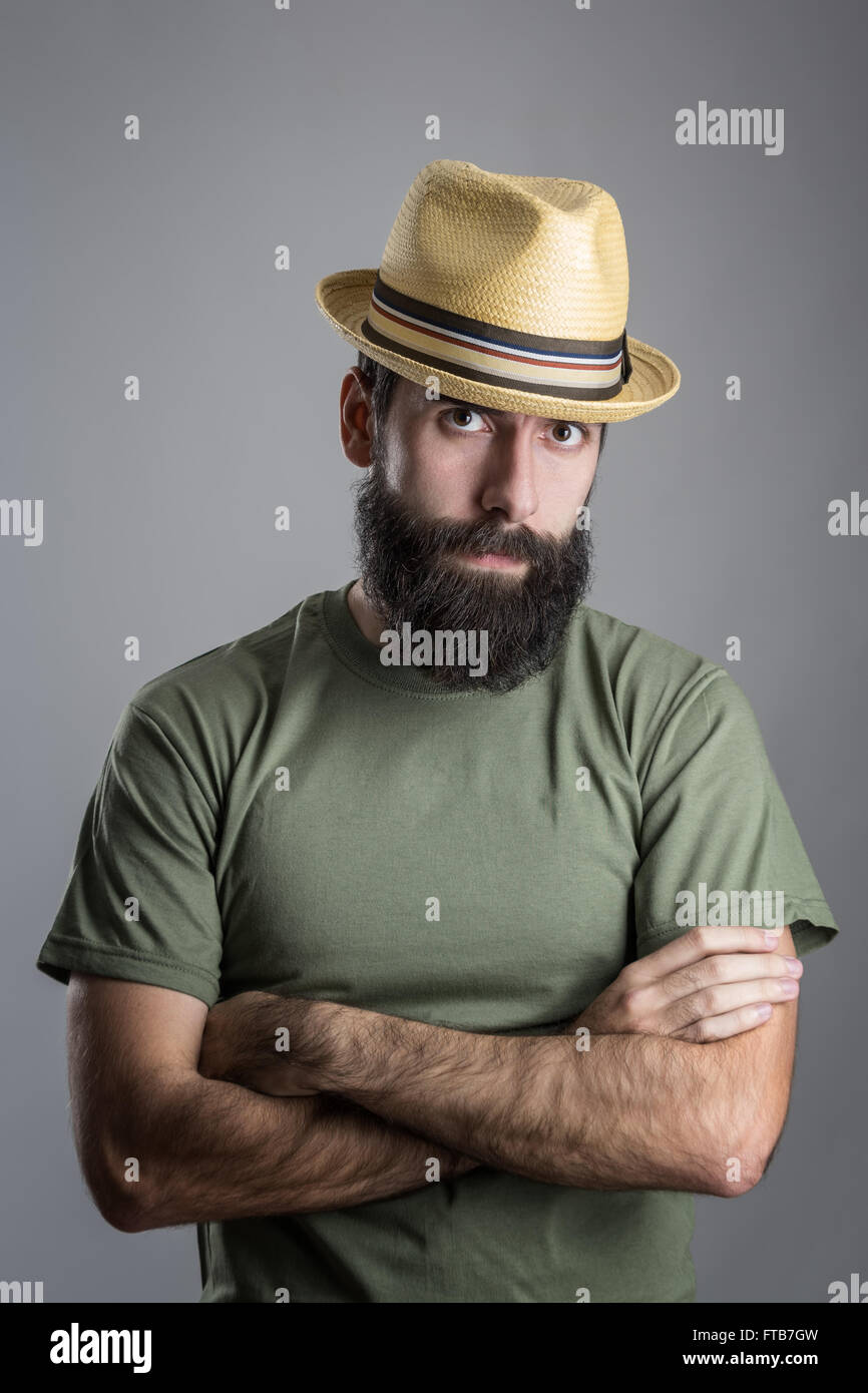 Serious unhappy bearded man with straw hat intense scowl at camera. Headshot portrait over gray studio background with vignette. Stock Photo