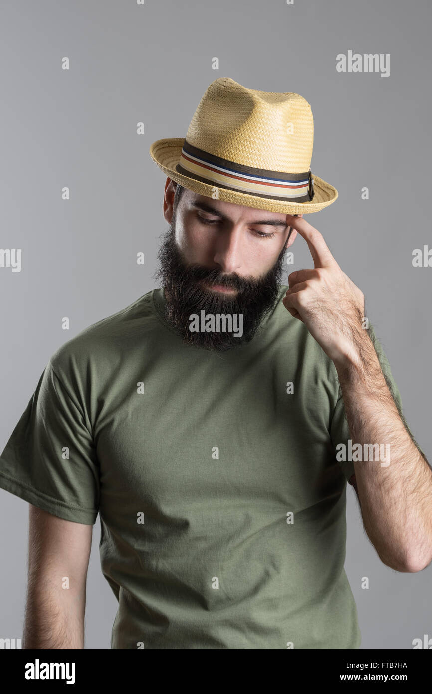 Worried thinking bearded man wearing straw hat looking down and scratching hand with finger. Portrait over gray background Stock Photo
