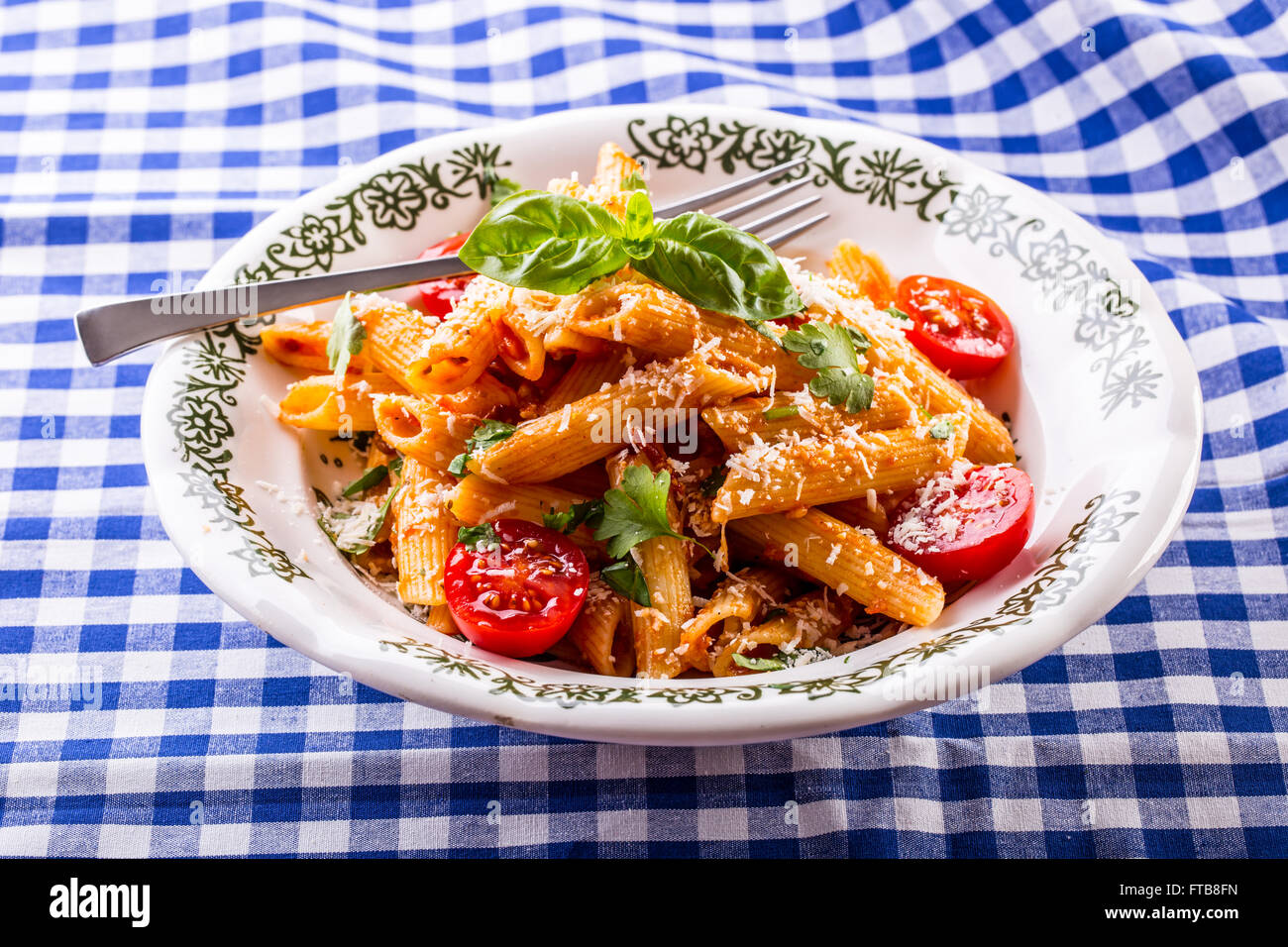 Plate with pasta pene Bolognese sauce cherry tomatoes parsley top and basil leaves on checkered blue tablecloth. Italian and Med Stock Photo