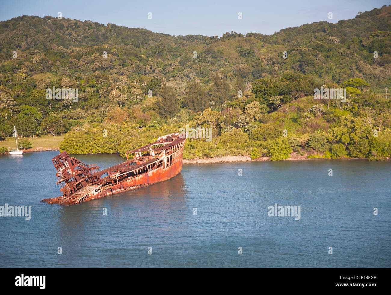 Sunken ship sitting in Mahogany Bar in Roatán, Honduras with the islands lush vegetation covering the hills in the background Stock Photo