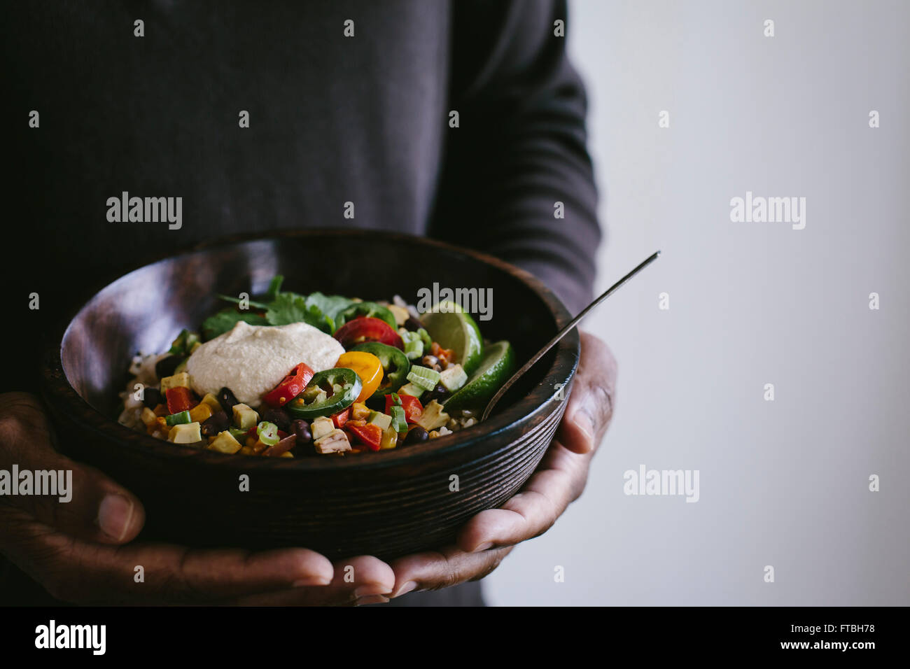 A man is holding a bowl of Mexican Burrito Bowl topped with cashew chipotle cream sauce. Stock Photo