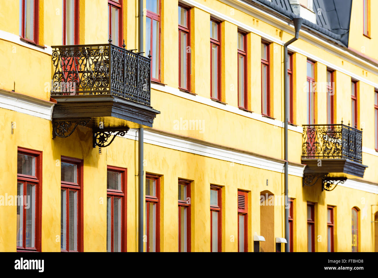 Two black metal balconies on a yellow building with red windows. Stock Photo