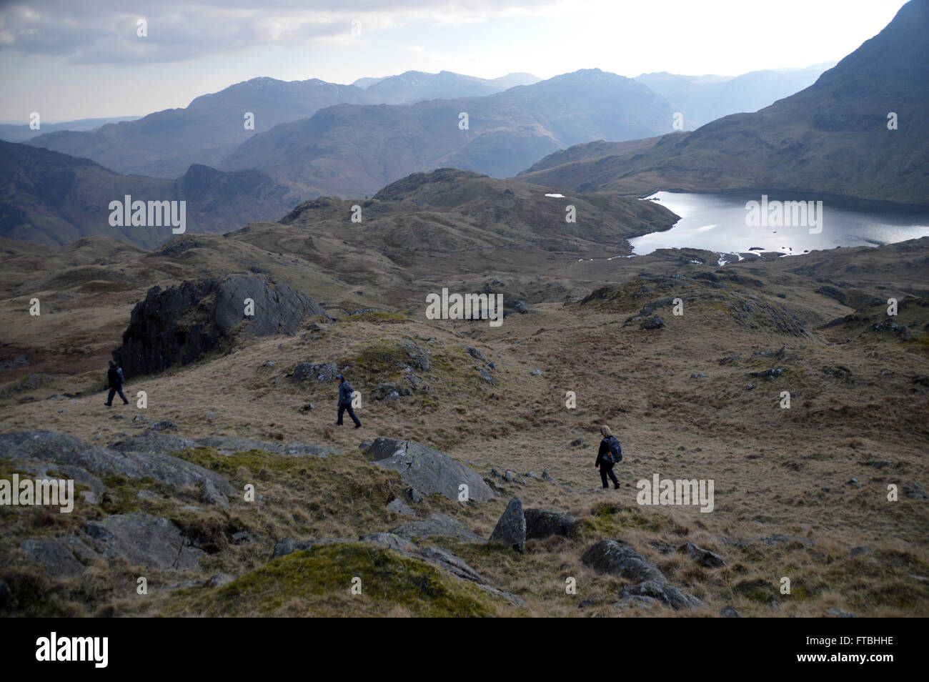 3 Fellwalkers Approaching Stickle Tarn from Sargent Man, Langdale Fells, Cumbria UK. Stock Photo