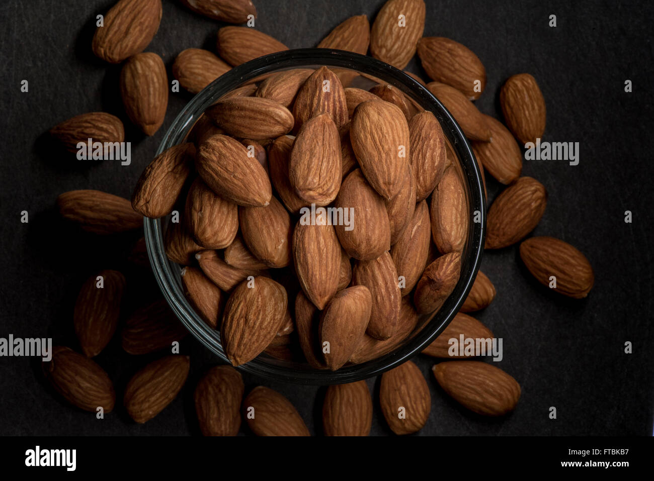 Whole Almonds Spill Over Glass Bowl with lighting on the center Stock Photo