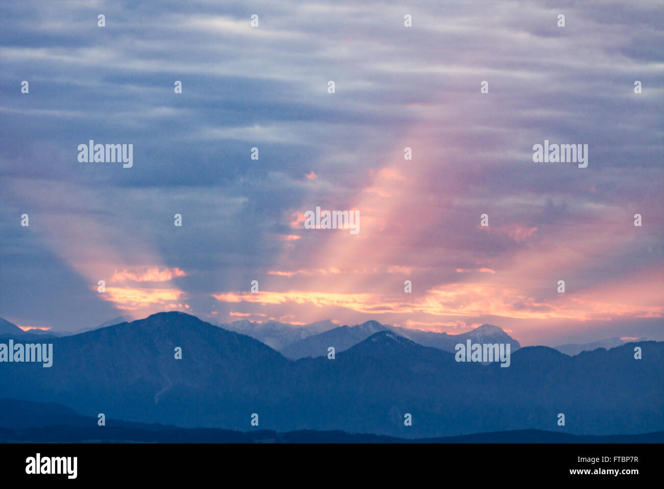 First rays of the rising sun on dawning cloudy sky over dark blue morning Alps mountains Stock Photo