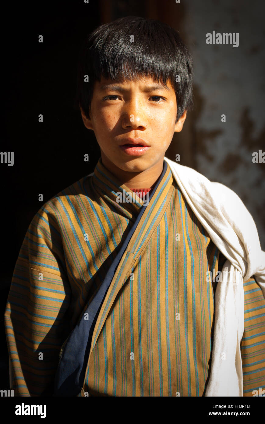 Portrait of a young Bhutanese boy wearing a traditional striped gho (robe) in Nimshong Village, southern Bhutan Stock Photo