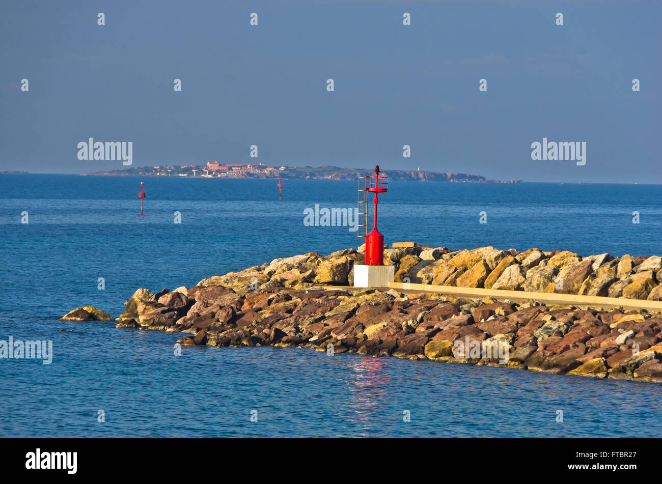 Red lighthouse at entrance to small ferry harbor in Sardinia Stock Photo