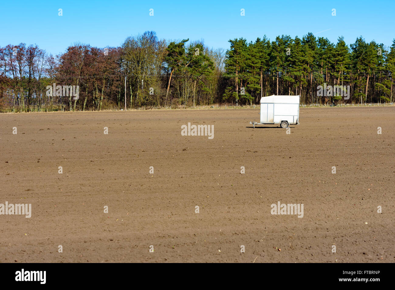 A deserted and abandoned horse trailer left on a harrowed farmers field in spring. Copy space in soil. Forest in background. Stock Photo