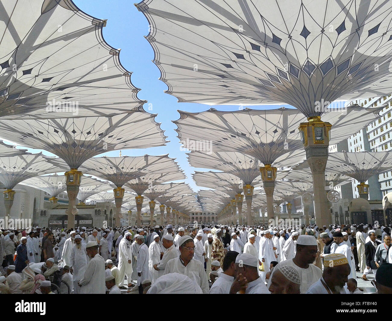 Thousands of Muslim hajj pilgrims rest and relax under the Masjid Nabwi  umbrellas in Mecca, al-Hejaz, Saudi Arabia. The high-tech giant sunshades  provide protection for pilgrims waiting to enter the Nabawi mosque