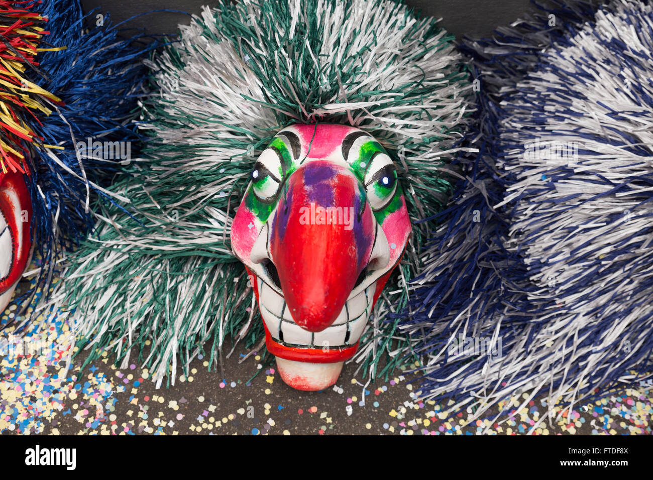 A single mask of a Waggis with a huge red nose and gray-green hair laying on the ground on top of colorful confetti Stock Photo