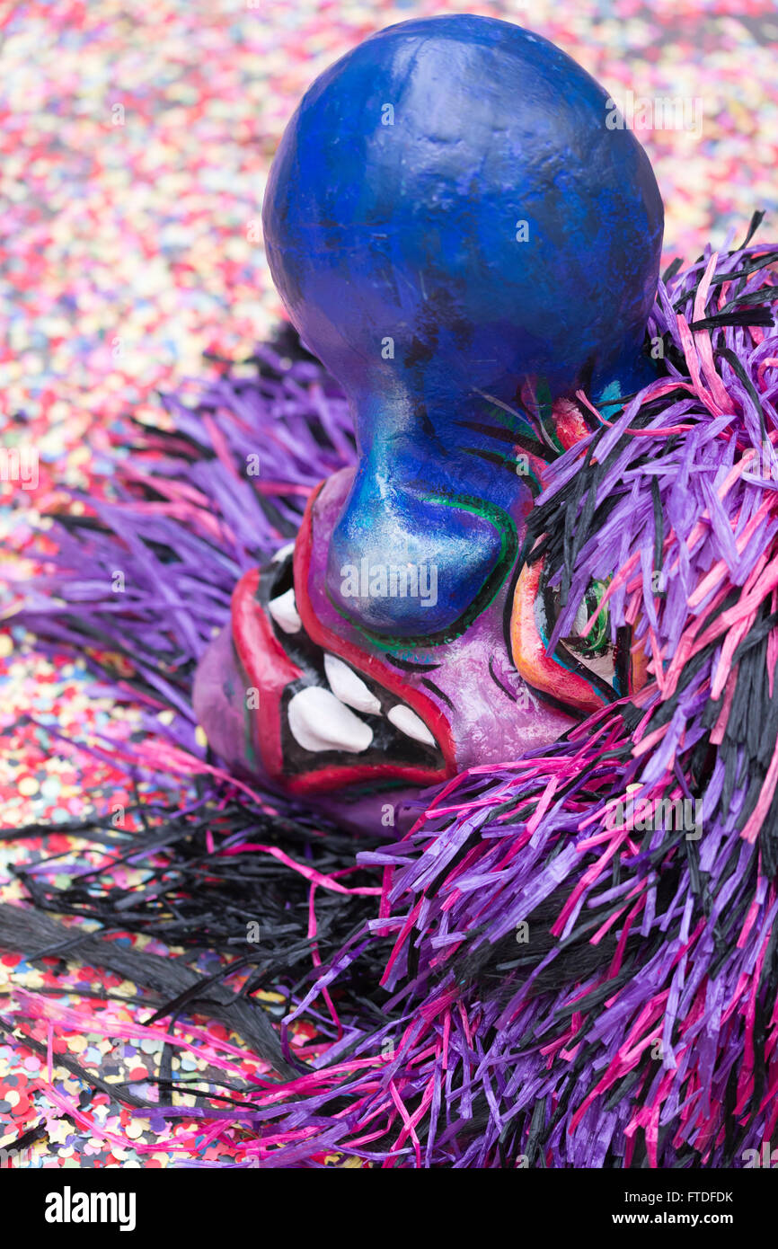 A single mask of a Waggis with a huge blue nose and pink-purple hair laying on the ground on top of colorful confetti. Stock Photo