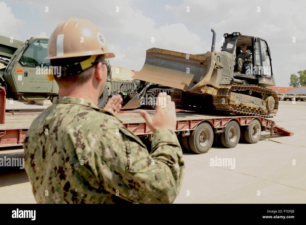 150907-N-SD965-092 ROTA, Spain (Sept. 7, 2015) Equipment Operator 1st Class Michael Yondolino, left, assigned to Naval Mobile Construction Battalion (NMCB) 1, signals directions to Equipment Operator 1st Class Christopher Harrison while he maneuvers a Caterpillar D6 dozer onto a semi-truck trailer in Naval Station Rota, Spain, Sept. 7, 2015. The Caterpillar D6 dozer was one of four pieces of equipment and two conex boxes that are being transported to a project site in support of NMCB 1’s operations in 6th Fleet. U.S. 6th Fleet, headquartered in Naples, Italy, conducts the full spectrum of join Stock Photo