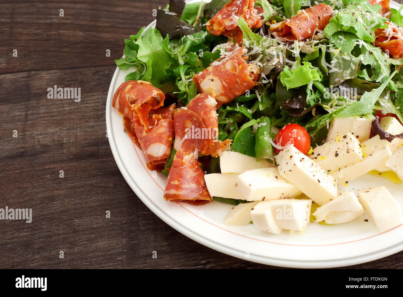 A plate of Italian salad with salami calabrese, cherry tomato, mozzarella, rucola, parmigiano and lemon. Stock Photo