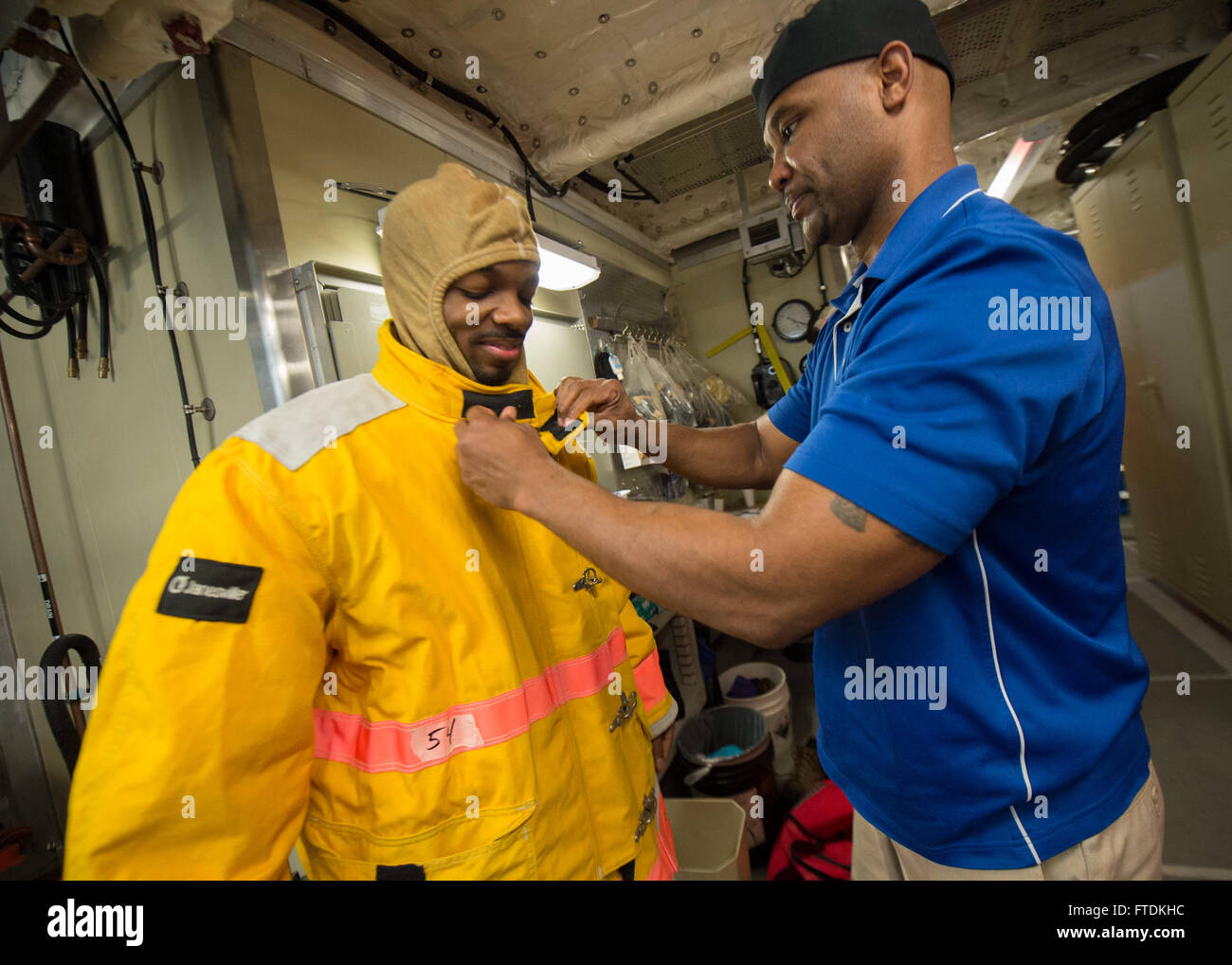160125-N-QF605-008 ATLANTIC OCEAN (Jan. 25, 2016) - Cook Baker Irvine Cummings helps Able Bodied Seaman David Leader don his personal protective gear during a fire drill aboard USNS Spearhead (T-EPF 1) Jan. 25, 2016. The Military Sealift Command expeditionary fast transport vessel USNS Spearhead is on a scheduled deployment to the U.S. 6th Fleet area of operations to support the international collaborative capacity-building program Africa Partnership Station. (U.S. Navy photo by Mass Communication Specialist 1st Class Amanda Dunford/Released) Stock Photo