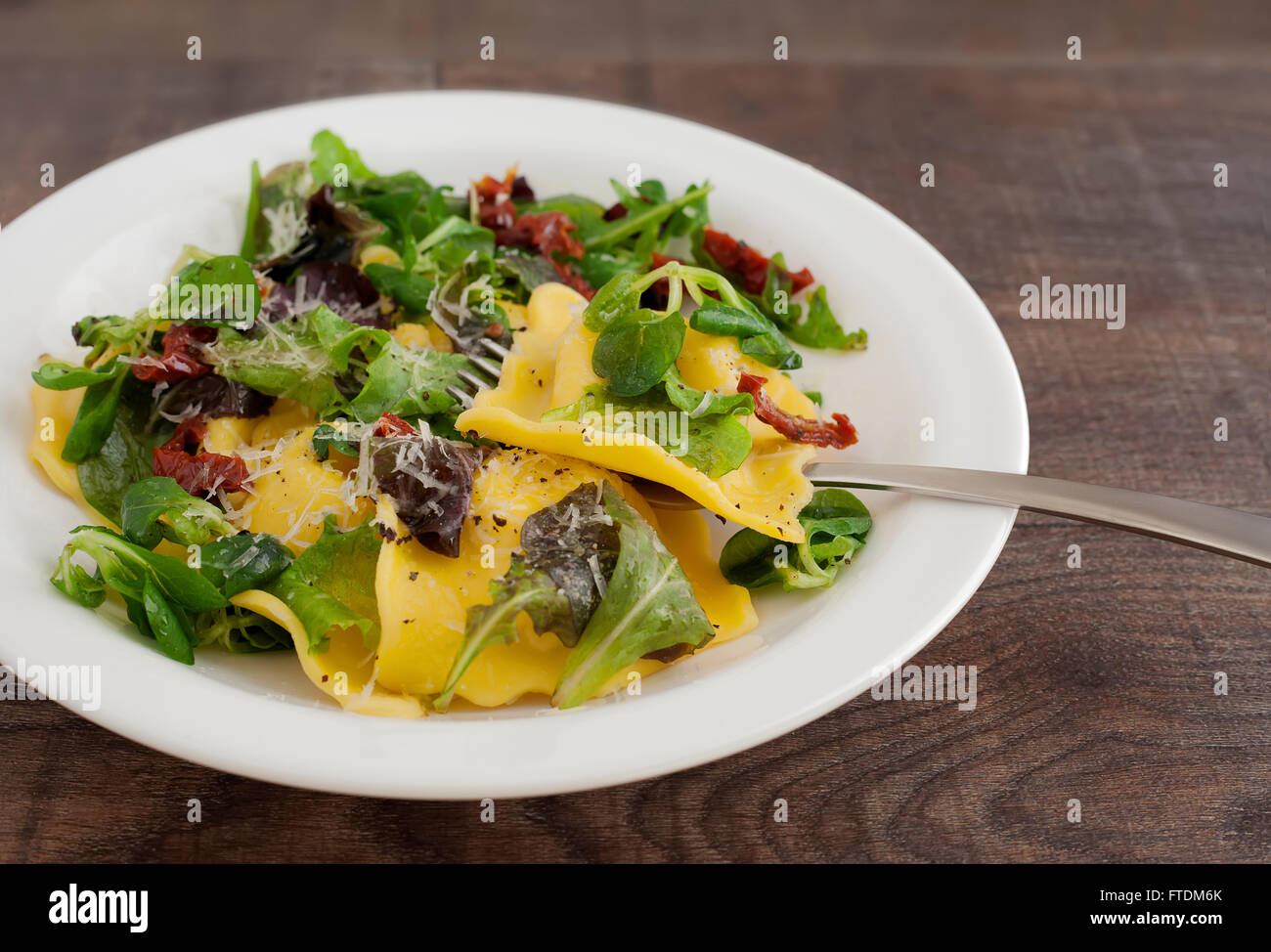 Italian cuisine ravioli with green salad, parmigiano cheese and sun dried tomato. Stock Photo