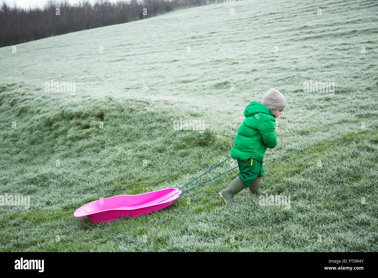 A little boy pulling his sledge back up the hill Stock Photo