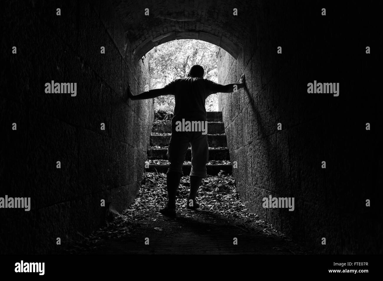 Young tired man leaves dark stone tunnel with glowing end, black and white photo Stock Photo