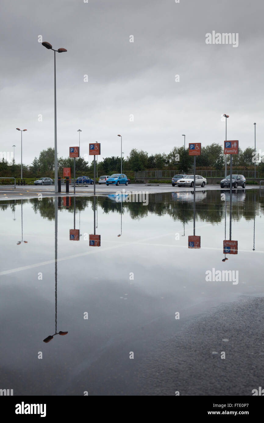 A car park flooded by heavy rain reflects the sky and the cars in a ...