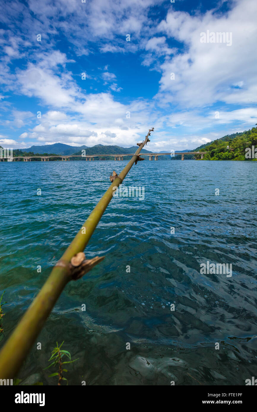 Fishing rod made of tree branch at a tropical lake and islands in cloudy blue sky. Belum resort, Banding, Temenggor Lake. Malays Stock Photo