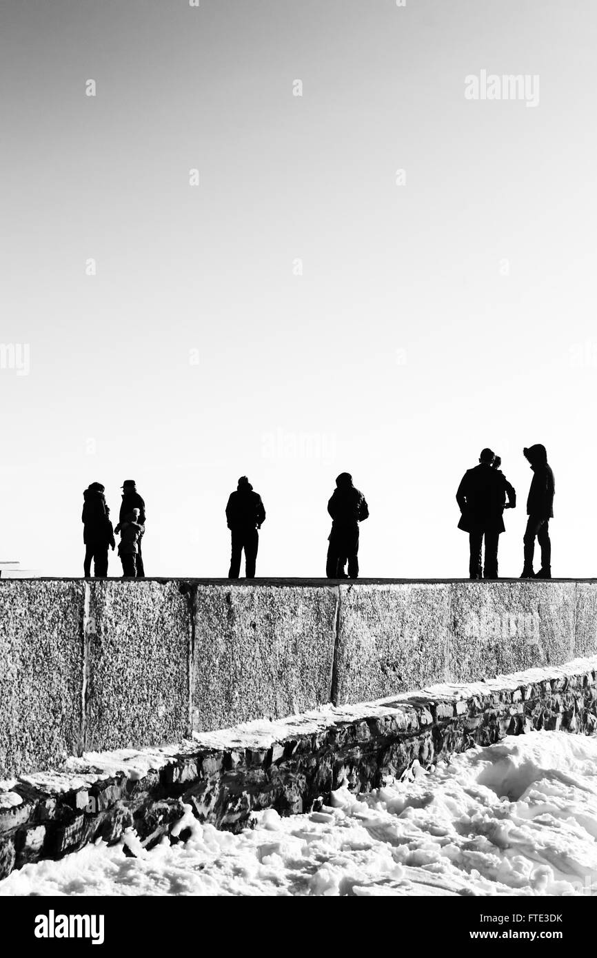 Groups of people stand on the edge of the horizon in a monochrome black and white abstract. Clear sky overhead adds to the sense Stock Photo