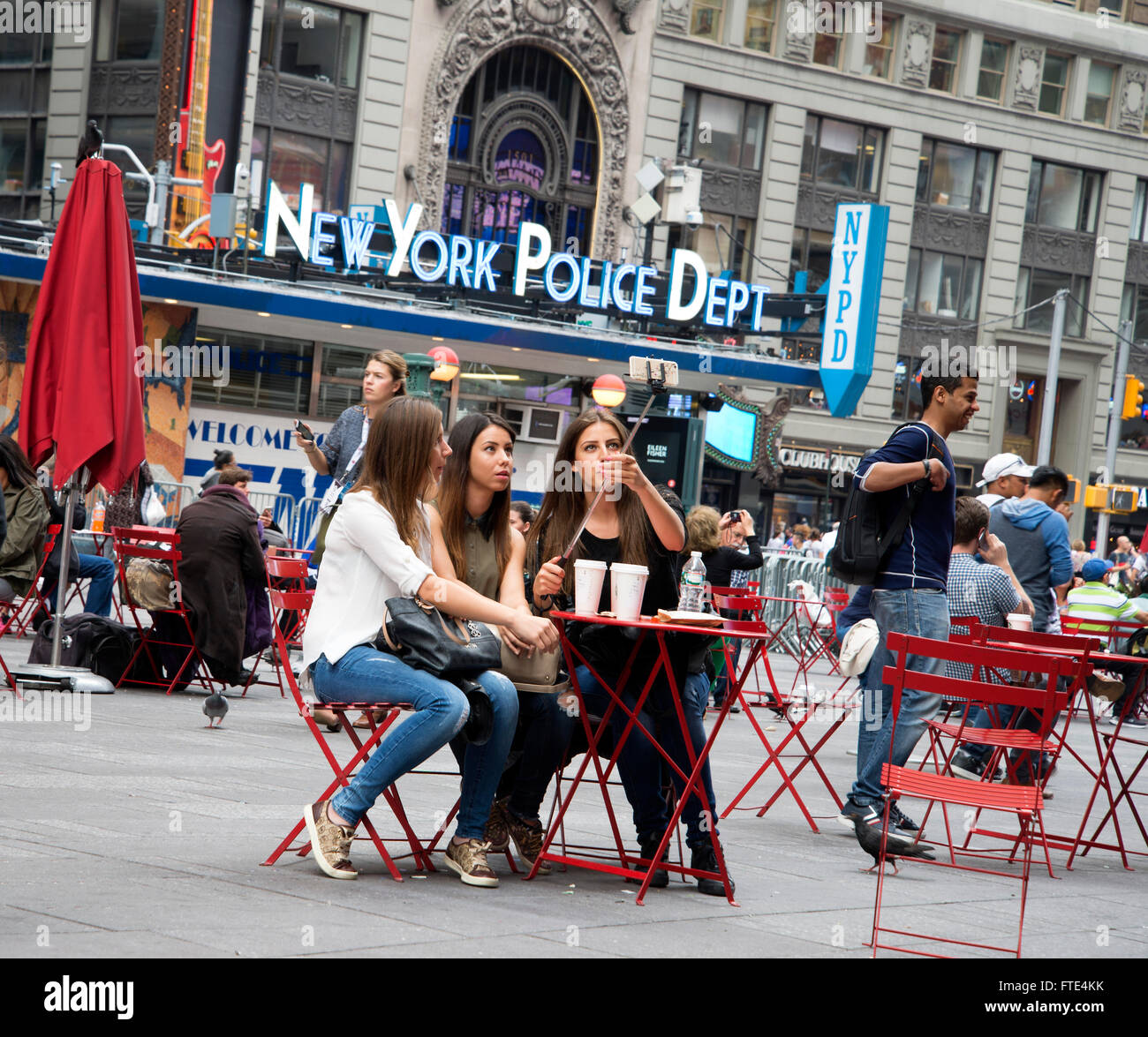 New York three teenagers sit table outside in Time Square taking photos using selfies click stick. Stock Photo
