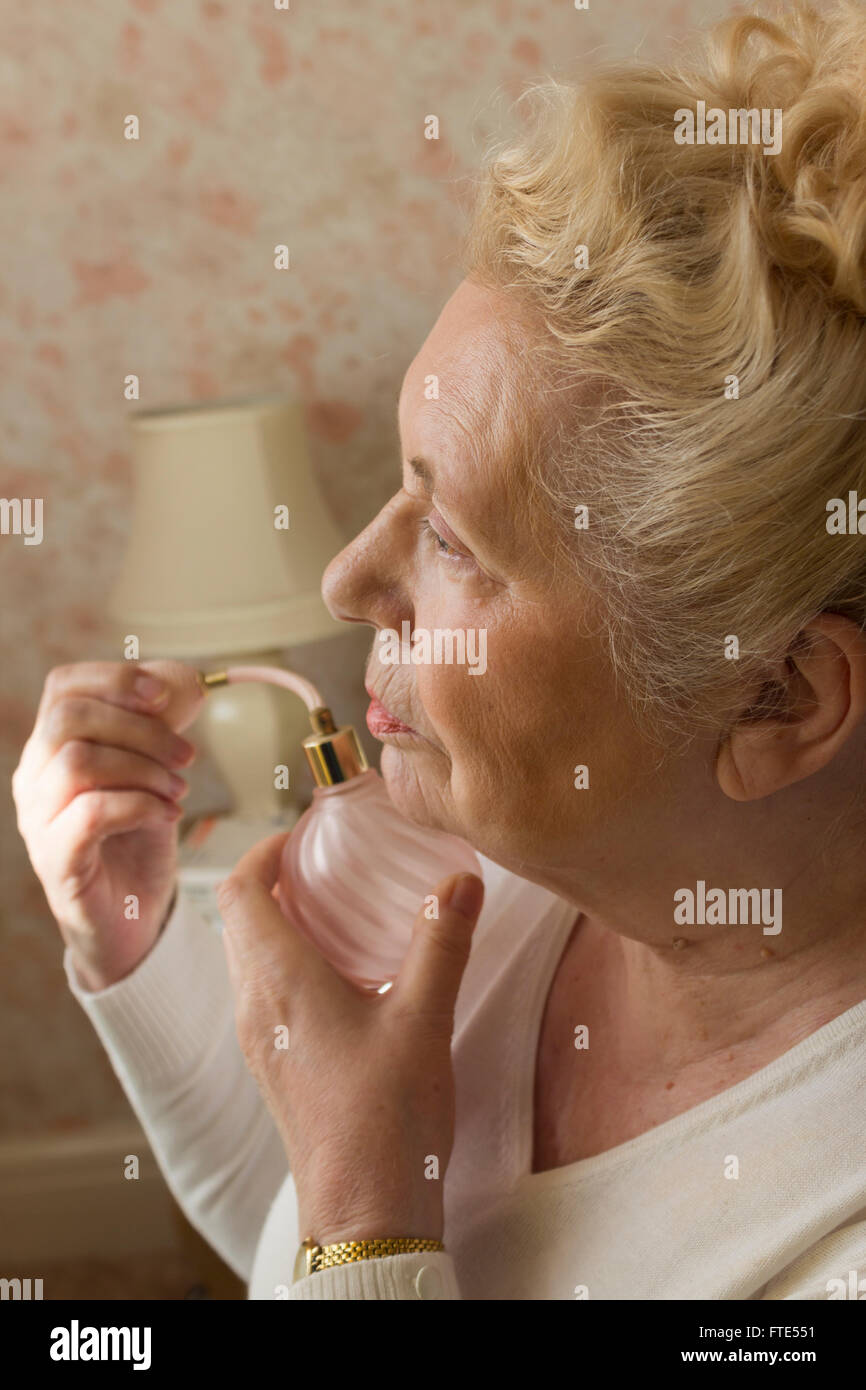 Elderly lady applying perfume from an old fashioned pink glass bottle. Stock Photo