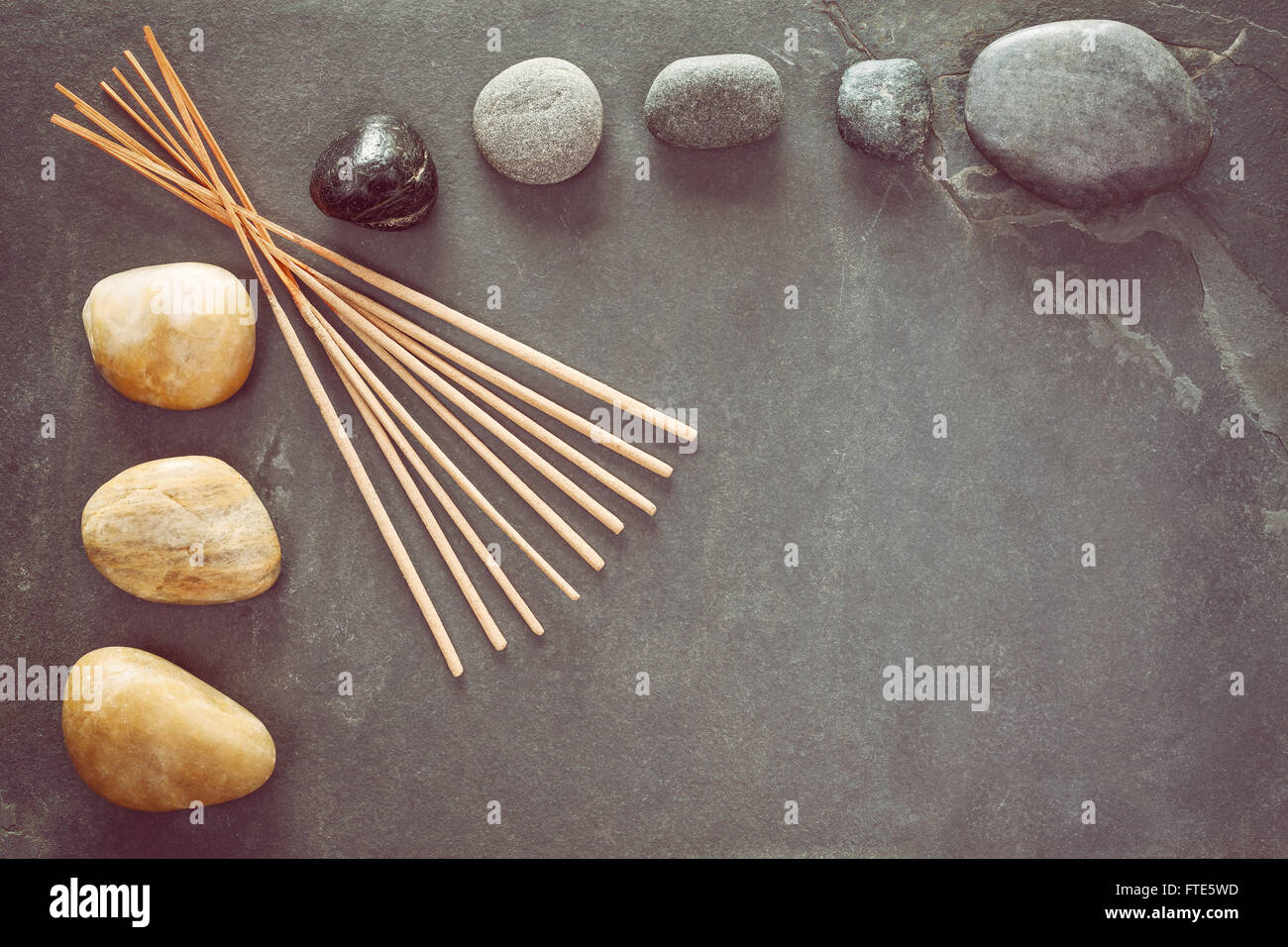 Retro toned stones on slate background with incense sticks, zen or spa and wellness background. Stock Photo