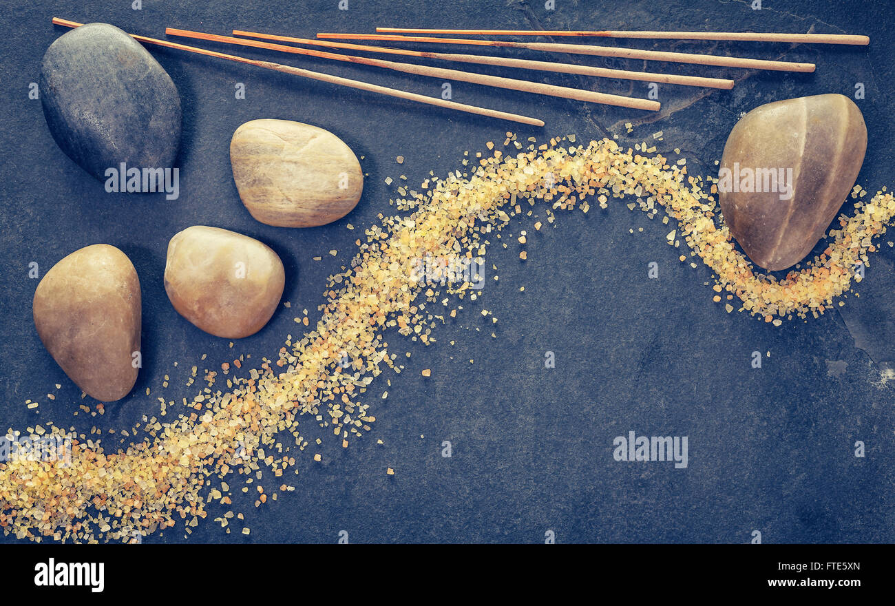 Vintage filtered stones on slate background with incense sticks and bath salts, zen or spa and wellness background. Stock Photo