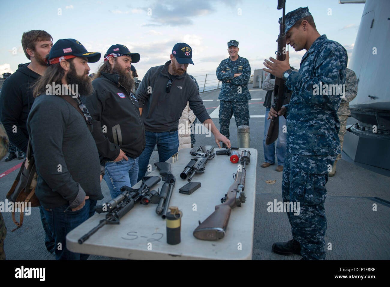 SOUDA BAY, Greece  (Dec. 07, 2013) -  Gunner's Mate 2nd Class Gregory Spaulding shows 'Duck Dynasty' stars Jep and Willie Robertson, and Washington Nationals baseball player Adam Laroche, the weapons that  the Arleigh Burke-class guided-missile destroyer USS Stout (DDG 55) has on board.  The demonstration is part of the annual USO holiday tour, which features a variety of other celebrities and the Chairman of the Joint Chiefs of Staff visiting bases and ships to interact with the crew for the holidays.  Stout, homeported in Norfolk, Va., is on a scheduled deployment supporting maritime securit Stock Photo