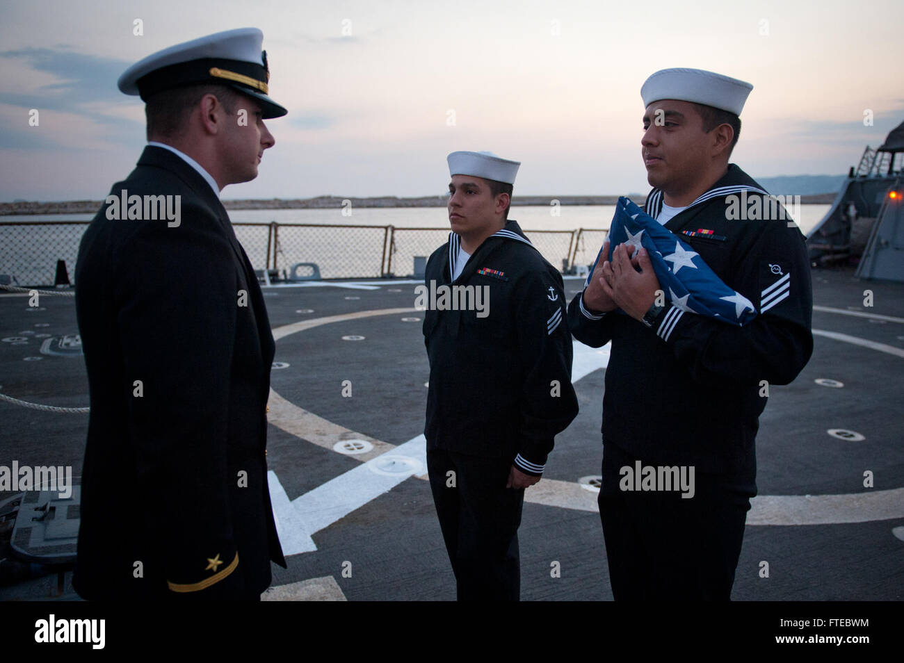 140312-N-WD757-068 MARSEILLE, France (March 12, 2014) – Operations Specialist Seaman Jose Garcia and Boatswain’s Mate Seaman Bryan Berrio prepare to turn over the national ensign after lowering the flag to Ensign Samuel Gasbarre during evening colors aboard the guided-missile destroyer USS Arleigh Burke (DDG 51) as the ship is in port on a scheduled visit to Marseille, France. Arleigh Burke is on a scheduled deployment in support of maritime security operations and theater security cooperation efforts in the U.S. 6th Fleet area of responsibility. (U.S. Navy photo by Mass Communication Speciali Stock Photo