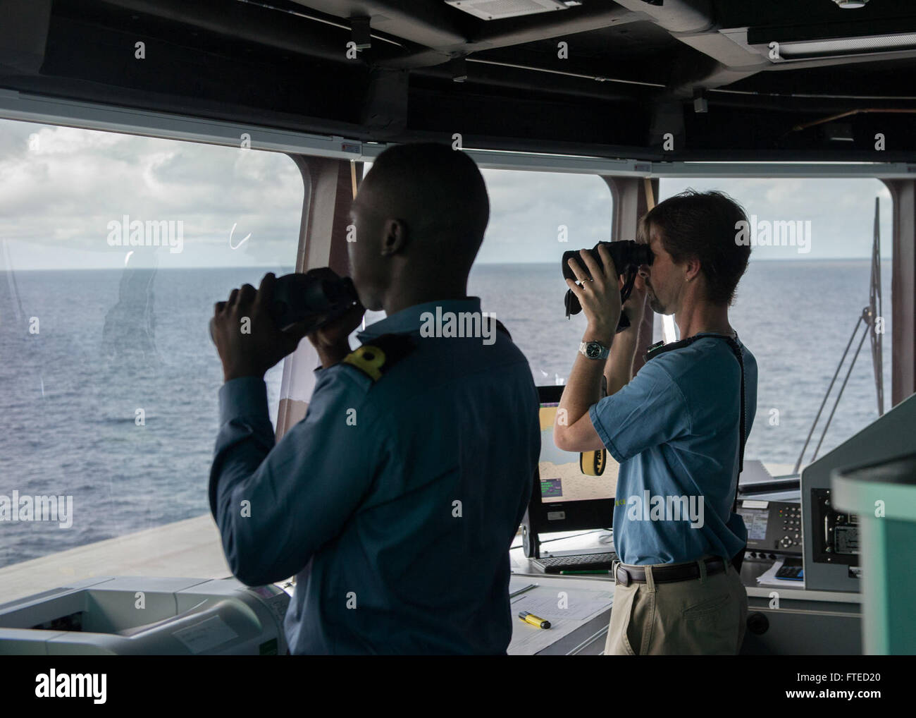 GULF OF GUINEA (April 2, 2014) - A Ghanaian sailor, left, and Captain Doug Casavant, civil service master aboard joint, high-speed vessel USNS Spearhead (JHSV 1) look through binoculars at a suspected illegal fishing vessel as part of a U.S.-Ghana combined maritime law enforcement operation under the African Maritime Law Enforcement Partnership (AMLEP) program as part of a U.S.-Ghana combined maritime law enforcement operation under the African Maritime Law Enforcement Partnership (AMLEP) program. AMLEP, the operational phase of Africa Partnership Station (APS), brings toget Stock Photo
