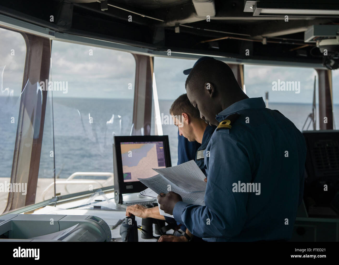GULF OF GUINEA (April 2, 2014) - A Ghanaian sailor, left, and Lt. Jeffrey Deitel, assigned to the U.S. Coast Guard law enforcement detachment, both embarked aboard joint, high-speed vessel USNS Spearhead (JHSV 1) check documents on a suspected illegal fishing vessel as part of a U.S.-Ghana combined maritime law enforcement operation under the African Maritime Law Enforcement Partnership (AMLEP) program. AMLEP, the operational phase of Africa Partnership Station (APS), brings together U.S. Navy, U.S. Coastguard, and respective Africa partner maritime forces to actively patro Stock Photo