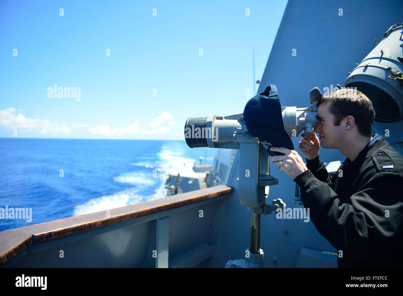 140709-N-AT101-088 ATLANTIC OCEAN (July 9, 2014) – Lt.j.g. Michael Pounders, assigned to the guided-missile destroyer USS Nitze (DDG 94), uses the ship-mounted binoculars to look for contacts in the distance while standing a navigation watch on the bridge wing. Nitze, homeported in Norfolk, Va., is conducting naval operations in support of U.S. national security interests in the U.S. 6th Fleet area of operations. (U.S. Navy photo by Mass Communication Specialist 1st Class Maddelin Angebrand) Stock Photo