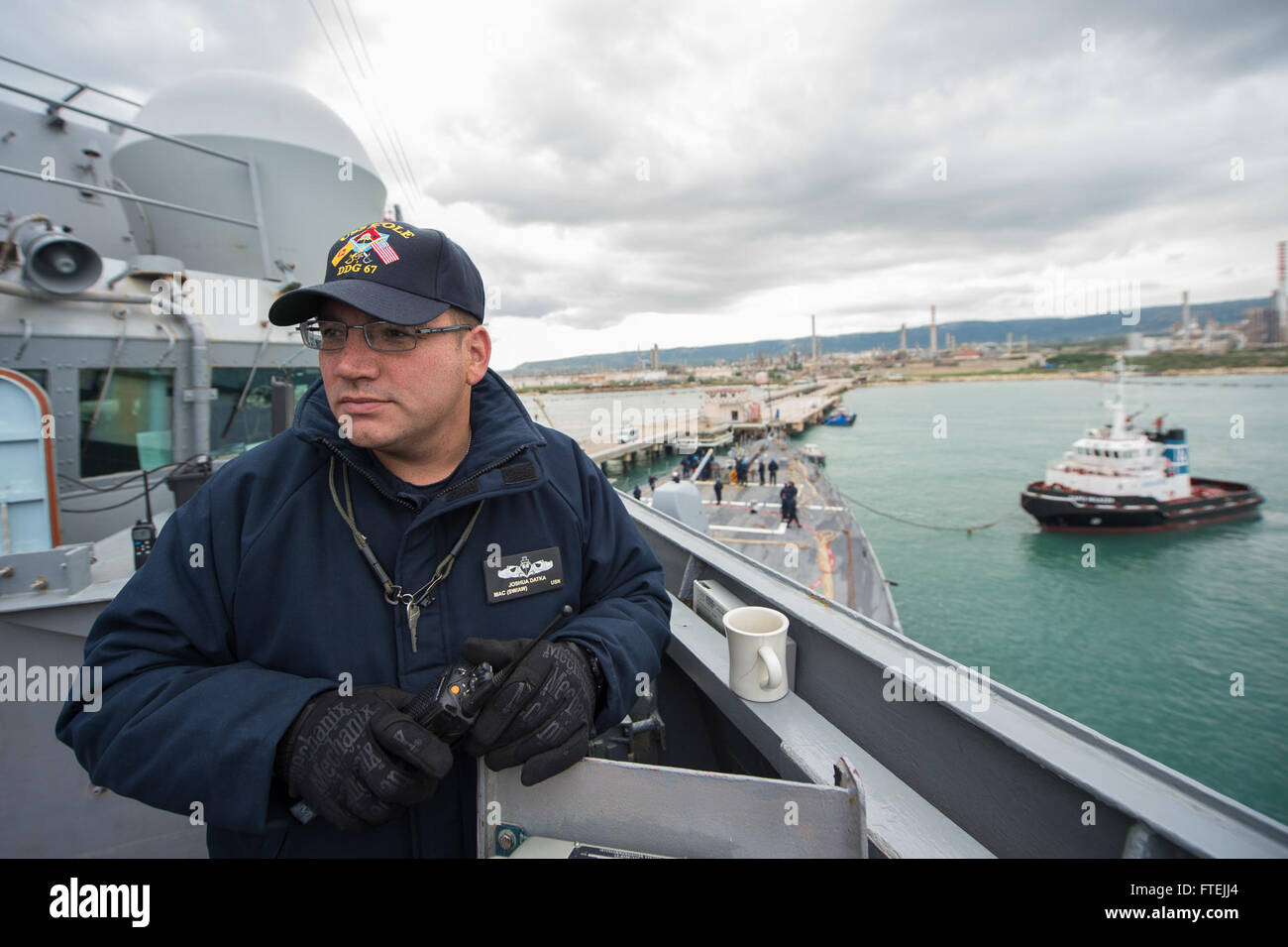 AUGUSTA BAY, Italy (Dec. 11, 2014) – Chief Master-at-Arms Joseph Datka, from Oconomowoc, Wisconsin, monitors civilian tugboats as USS Cole (DDG 67) departs Augusta Bay following a scheduled port visit Dec. 11 2014. Cole, an Arleigh Burke-class guided-missile destroyer, homeported in Norfolk, is conducting naval operations in the U.S. 6th Fleet area of operations in support of U.S. national security interests in Europe. Stock Photo