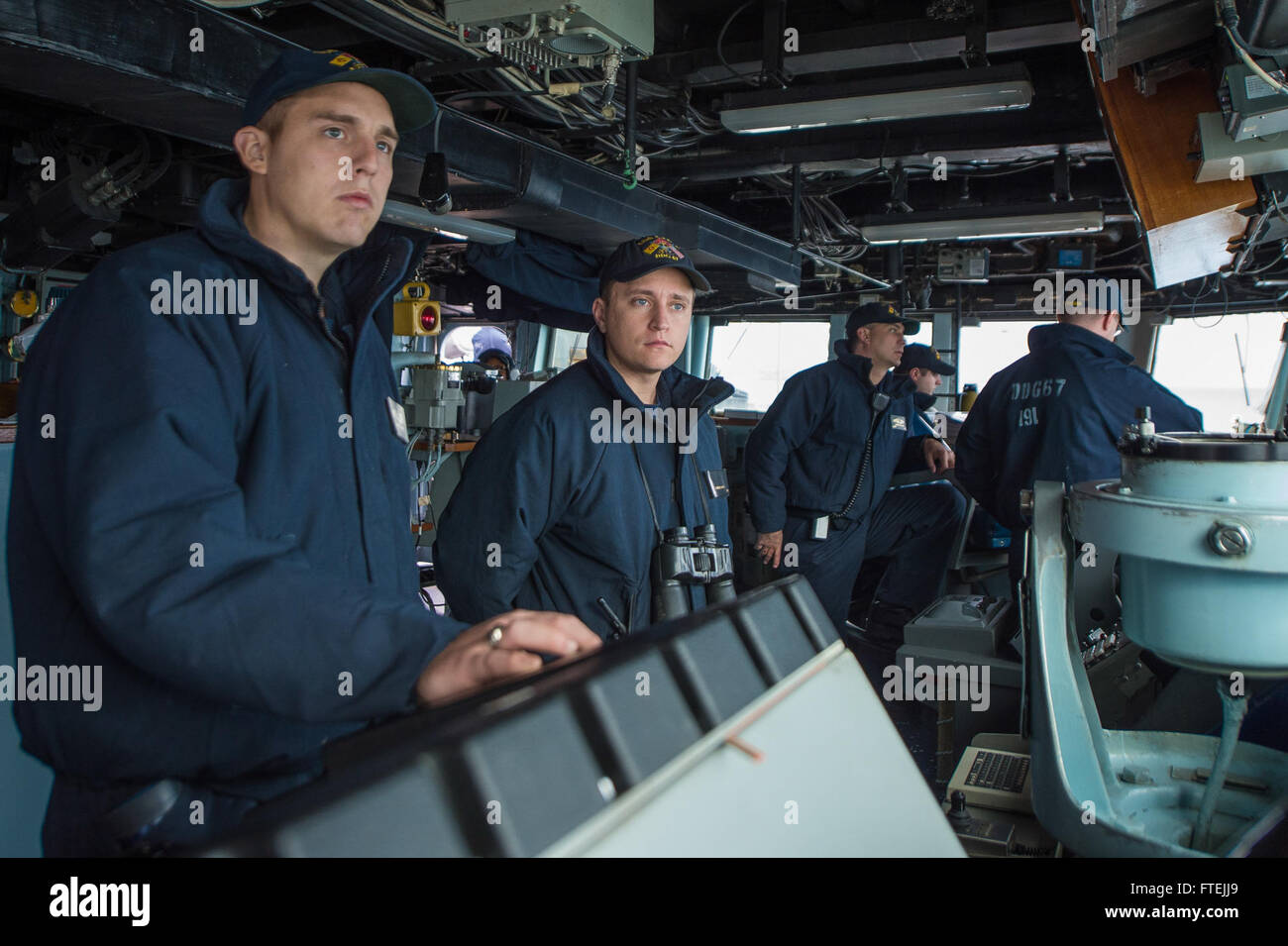 AUGUSTA BAY, Italy (Dec. 11, 2014) – Ensign Samuel Hadik, center, from Chester, New Hampshire, monitors oncoming civilian merchant traffic as USS Cole (DDG 67) departs Augusta Bay following a scheduled port visit Dec. 11 2014. Cole, an Arleigh Burke-class guided-missile destroyer, homeported in Norfolk, is conducting naval operations in the U.S. 6th Fleet area of operations in support of U.S. national security interests in Europe. Stock Photo