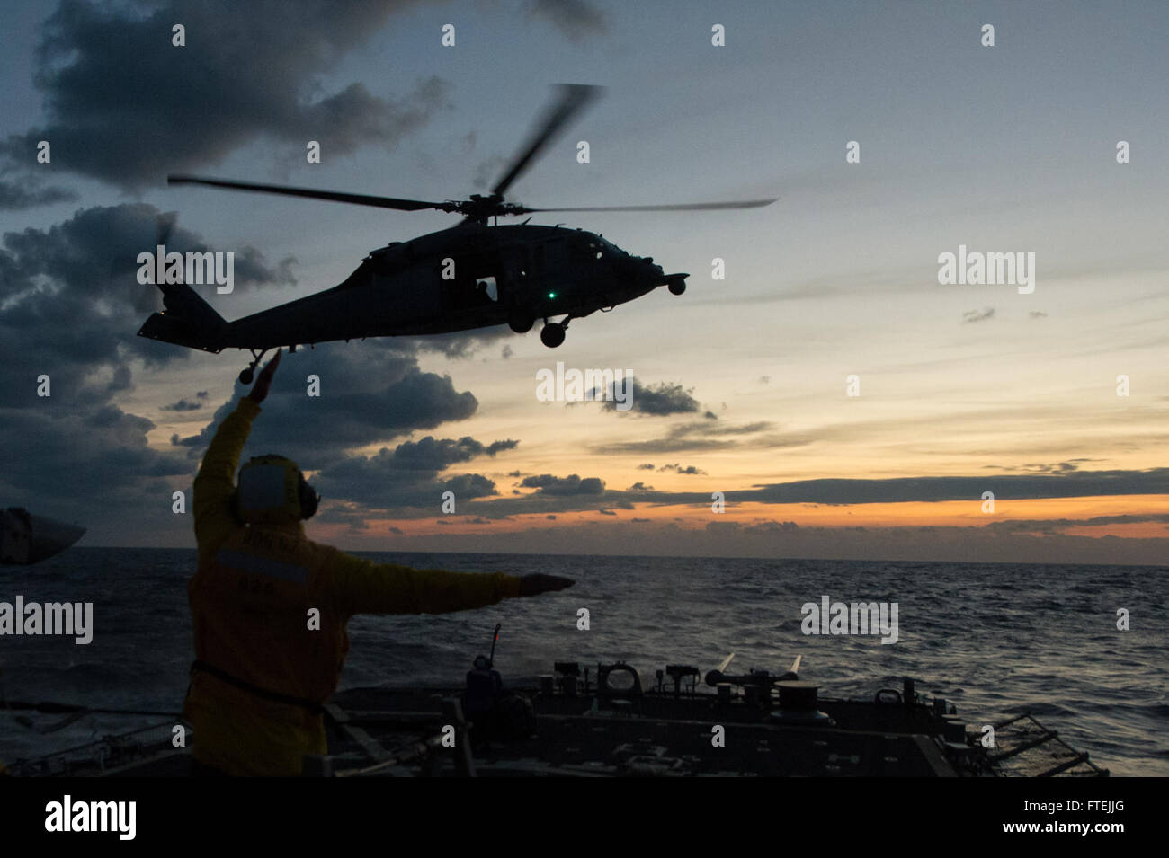 MEDITERRANEAN SEA (Dec. 11, 2014) – Boatswain’s Mate 3rd Class Dontrell Dorsett, from Fort Worth, Texas, directs nn MH 60S Sea Hawk helicopter attached to the Dragon Whales of Helicopter Sea Combat Squadron (HSC) 28 outboard of USS Cole (DDG 67) during deck-landing qualifications, Dec. 11 2014. Cole, an Arleigh Burke-class guided-missile destroyer, homeported in Norfolk, is conducting naval operations in the U.S. 6th Fleet area of operations in support of U.S. national security interests in Europe. Stock Photo