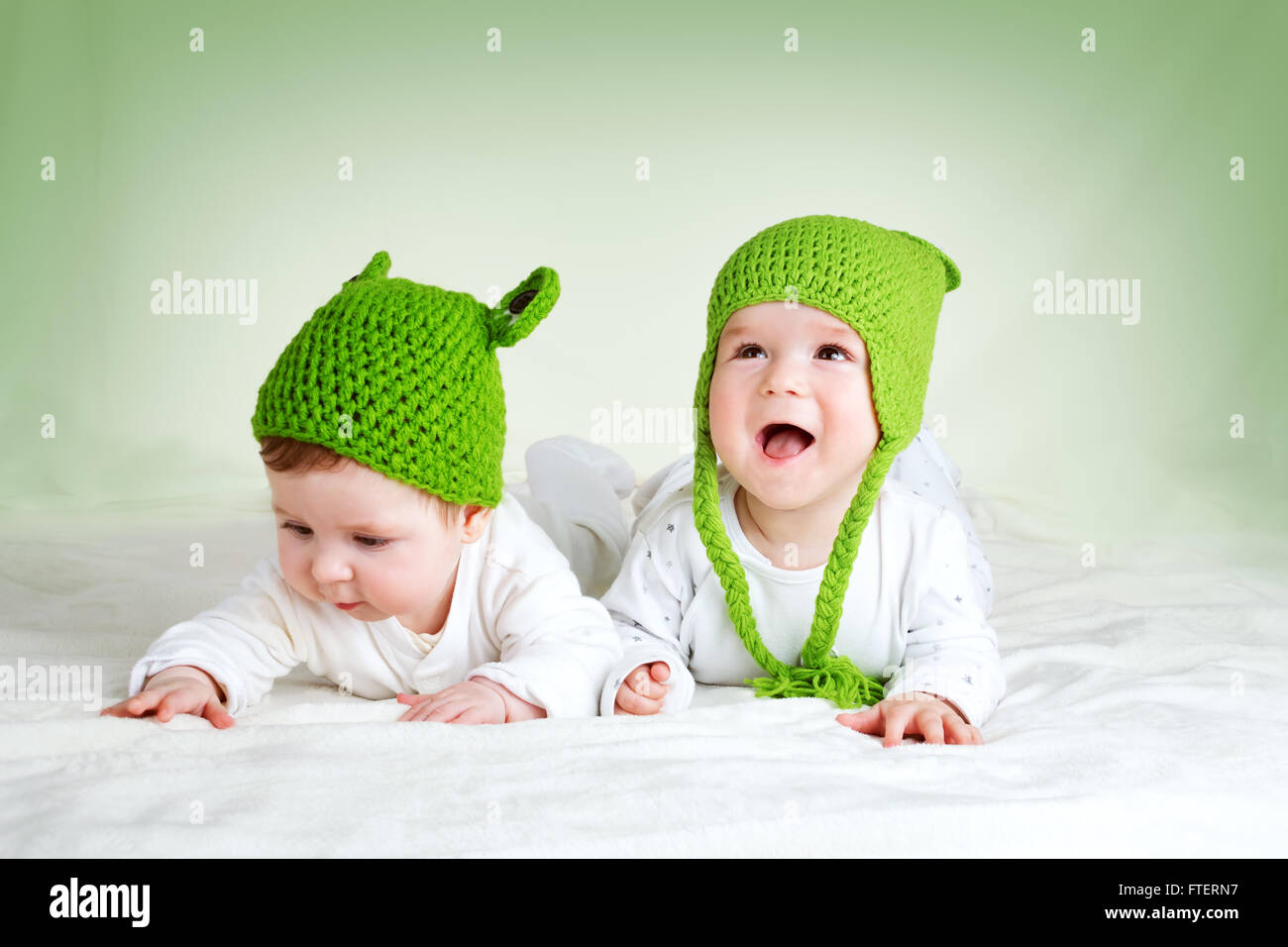 two cute babies lying in frog hats on spft blanket Stock Photo