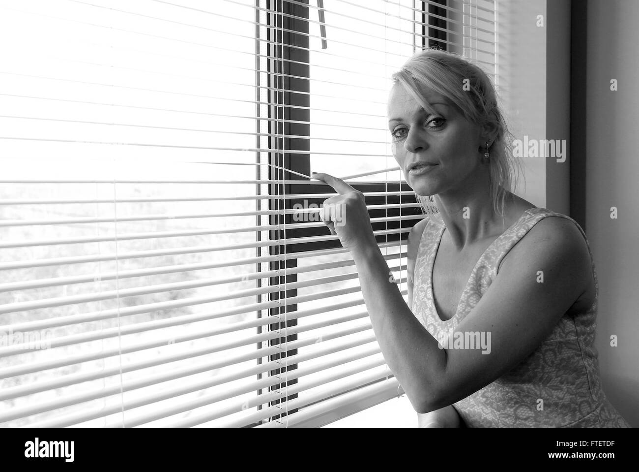 Beautiful blonde Eastern European mature woman looking expectantly out through venetian blinds. 2nd January 2015 Stock Photo
