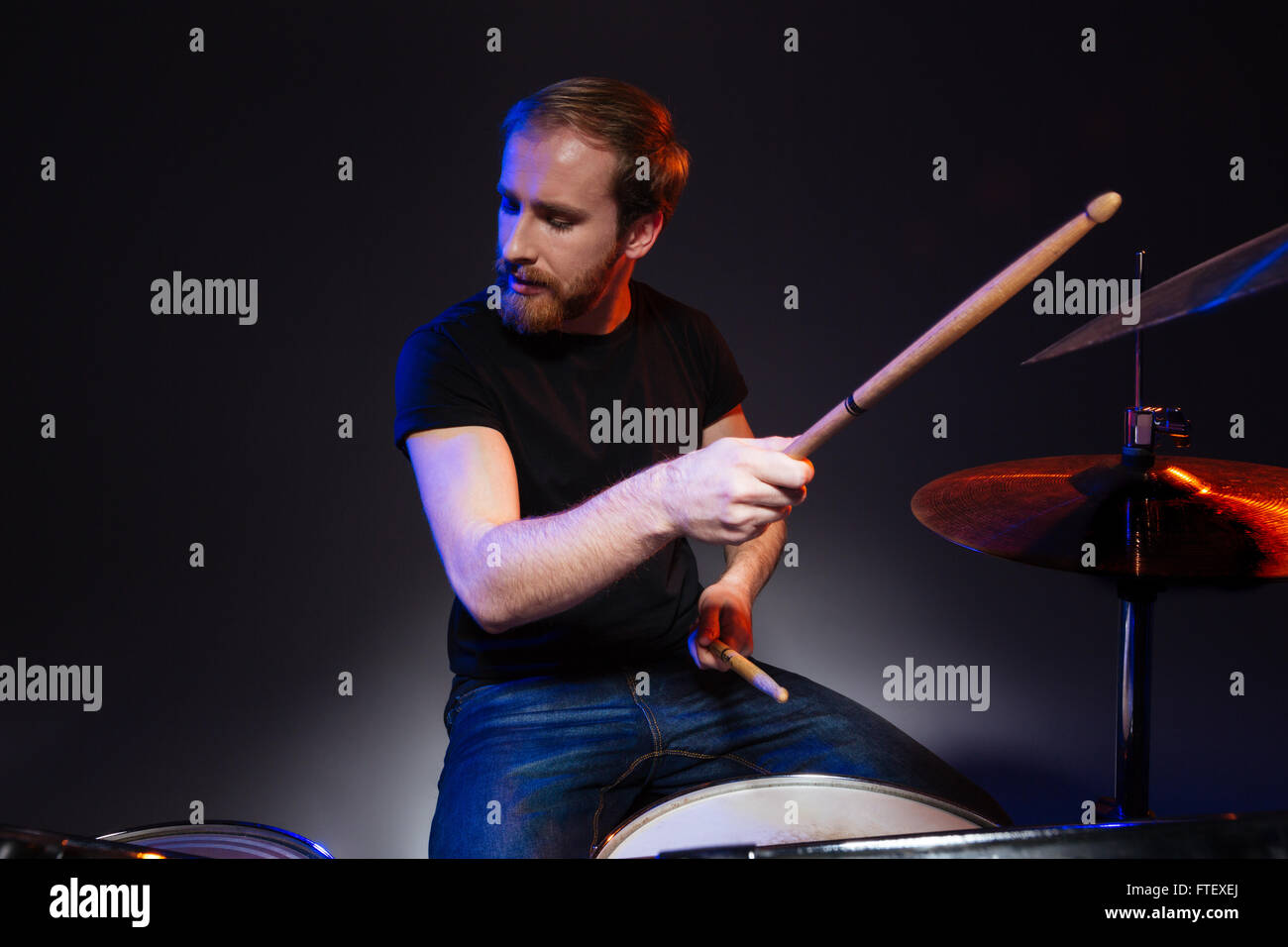 Bearded young man drummer with closed eyes sitting and playing drums ...
