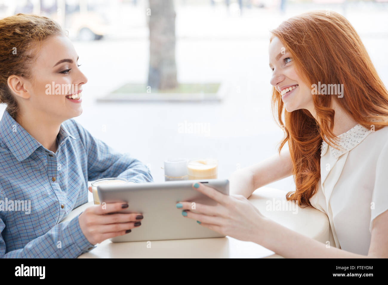 Two cheerful pretty young women using tablet in cafe together Stock ...