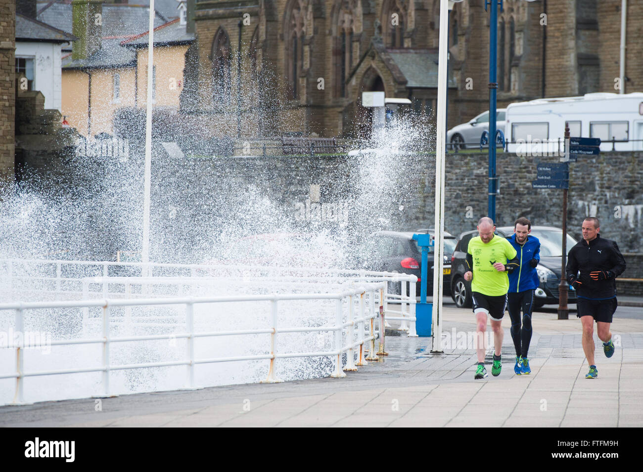 Aberystwyth Wales UK, Easter Monday,  28 March 2016   UK Weather: The strong winds associated with Storm Katie, the latest named storm of the 2015-16 season brings huge waves to batter the seafront at Aberystwyth.  A group of runners get splashed by the spary  The storm has wrought much damage , specially along the south facing coasts of England, with winds  gusting up to over 100mph in some places in the extreme south west    Credit:  keith morris/Alamy Live News Stock Photo