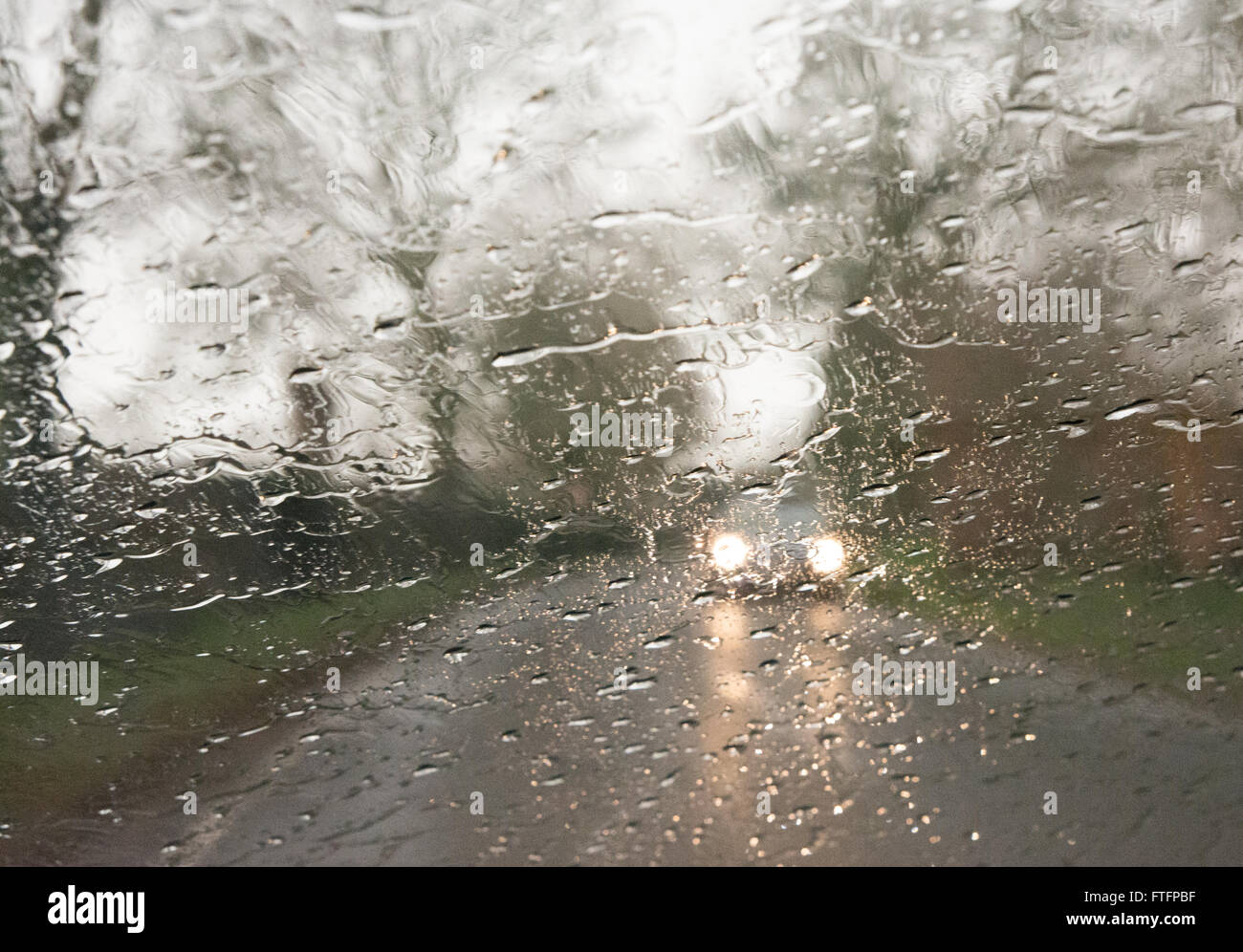 Rain on a car windscreen with oncoming headlights. Stock Photo