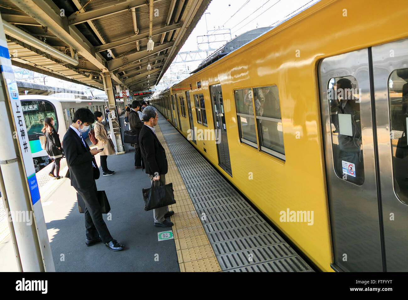 Passengers wait to aboard a yellow Seibu train at Kami-Shakujii station on March 29, 2016, Tokyo, Japan. Seibu Railway corporation announced that they will rent out entire carriages for party groups, on its Seibu Shinjuku, Ikebukuro, Hajima and Kokubunji Lines, allowing the group to choose which station to be picked up at and to be dropped off at. The special party service is aimed at alumni groups especially those that previously studied and commuted along one of the lines. In collaboration with Syoya Inc., a company specialised in organising alumni parties, the train company is taking bookin Stock Photo