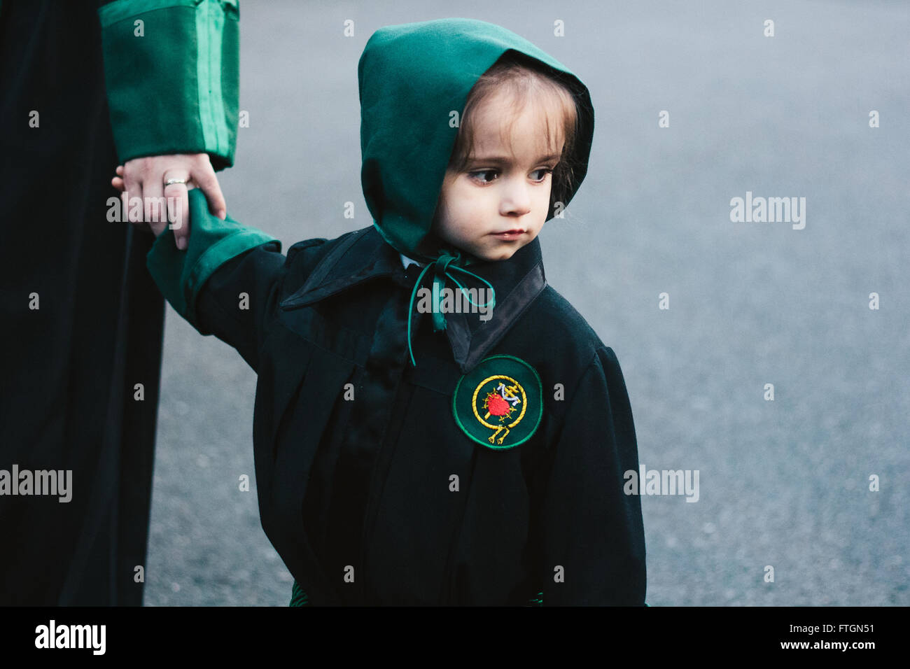 Little girl with a green hood and black tunic taking part in a procession during Holy Week, Spain. Stock Photo